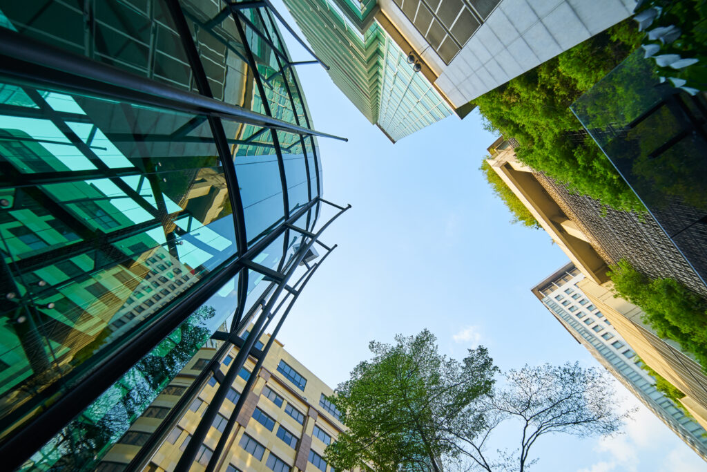 Low angle shot of modern glass buildings and green with clear sky background.